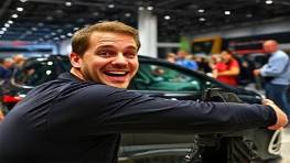 cutting-edge ABS technology, excited expression, demonstrating, photorealistic, at a car expo with curious onlookers, highly detailed, rotating displays, UHD resolution, sleek black, spotlight lighting, shot with a wide-angle lens.