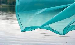 pliable plastic sheets, semi-transparent, fluttering, photorealistic, open-air workshop by a riverside, highly detailed, interaction with breeze and water reflections, teal and gray, diffused daylight, shot with a 35mm lens